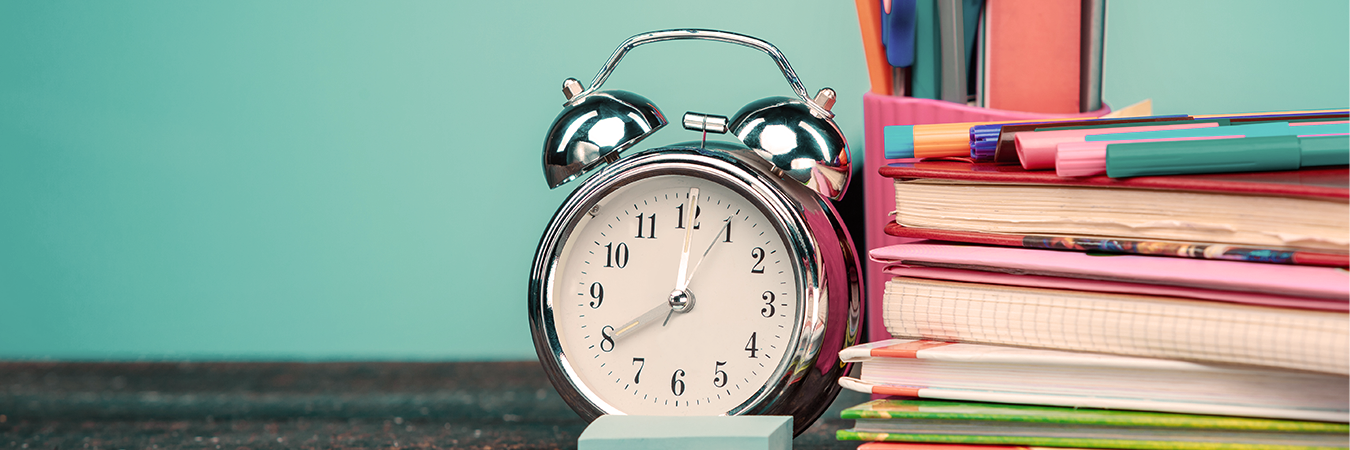 Eine Uhr steht auf einem Tisch mit Büchern und Stiften